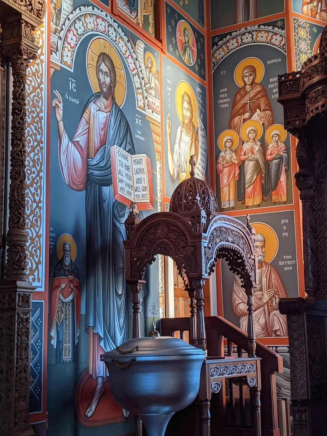 Orthodox church interior with floor-to-ceiling frescoes and carved wooden furnishings