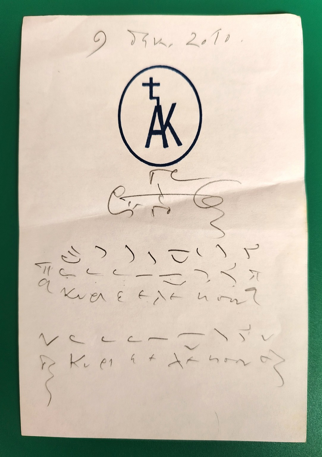 The full original photograph of Professor G. Stathis’s handwritten Kyrie Eleison on Sinai monastery memo paper, resting on a green surface
